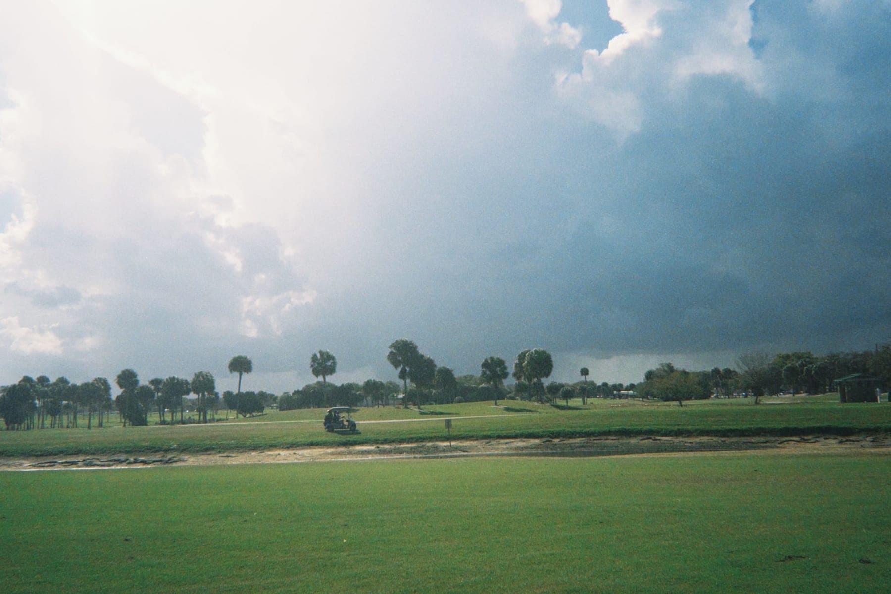 Dark storm clouds gathering over a golf course fairway, with a golf cart on the path